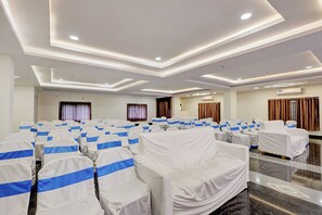 Un salón de conferencias con filas de sillas cubiertas en blanco y azul, piso pulido e iluminación empotrada en el techo.