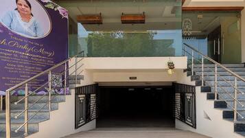 Entrada de hotel con fachada de vidrio, una escalera con barandales metálicos y un cartel de bienvenida.
