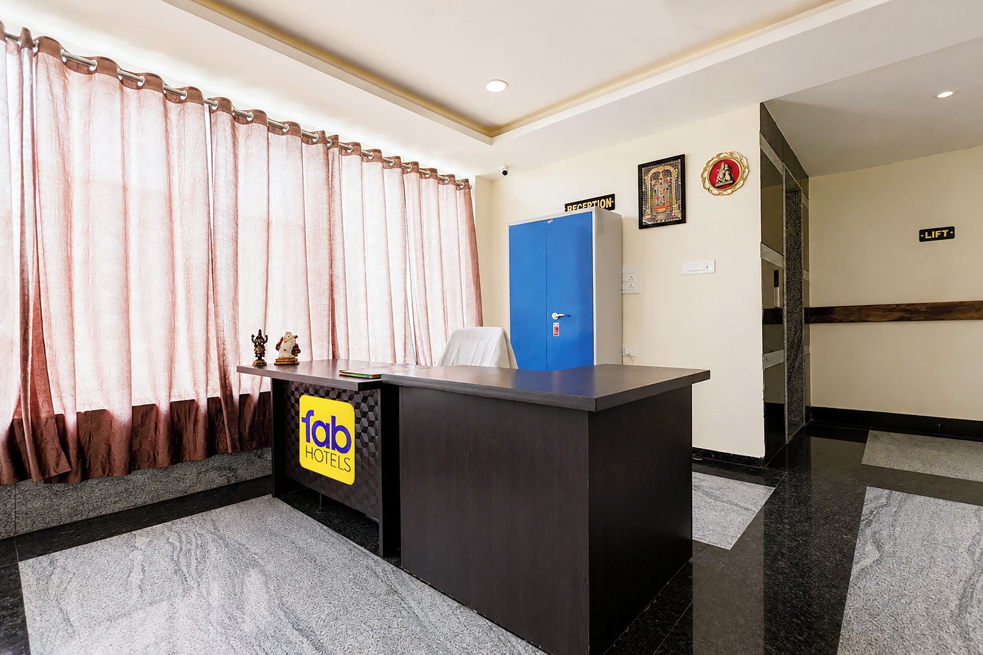 Una recepción con un letrero de 'fab hotels', una puerta azul con la leyenda 'RECEPTION' y un letrero de 'ASCENSOR' en la pared.