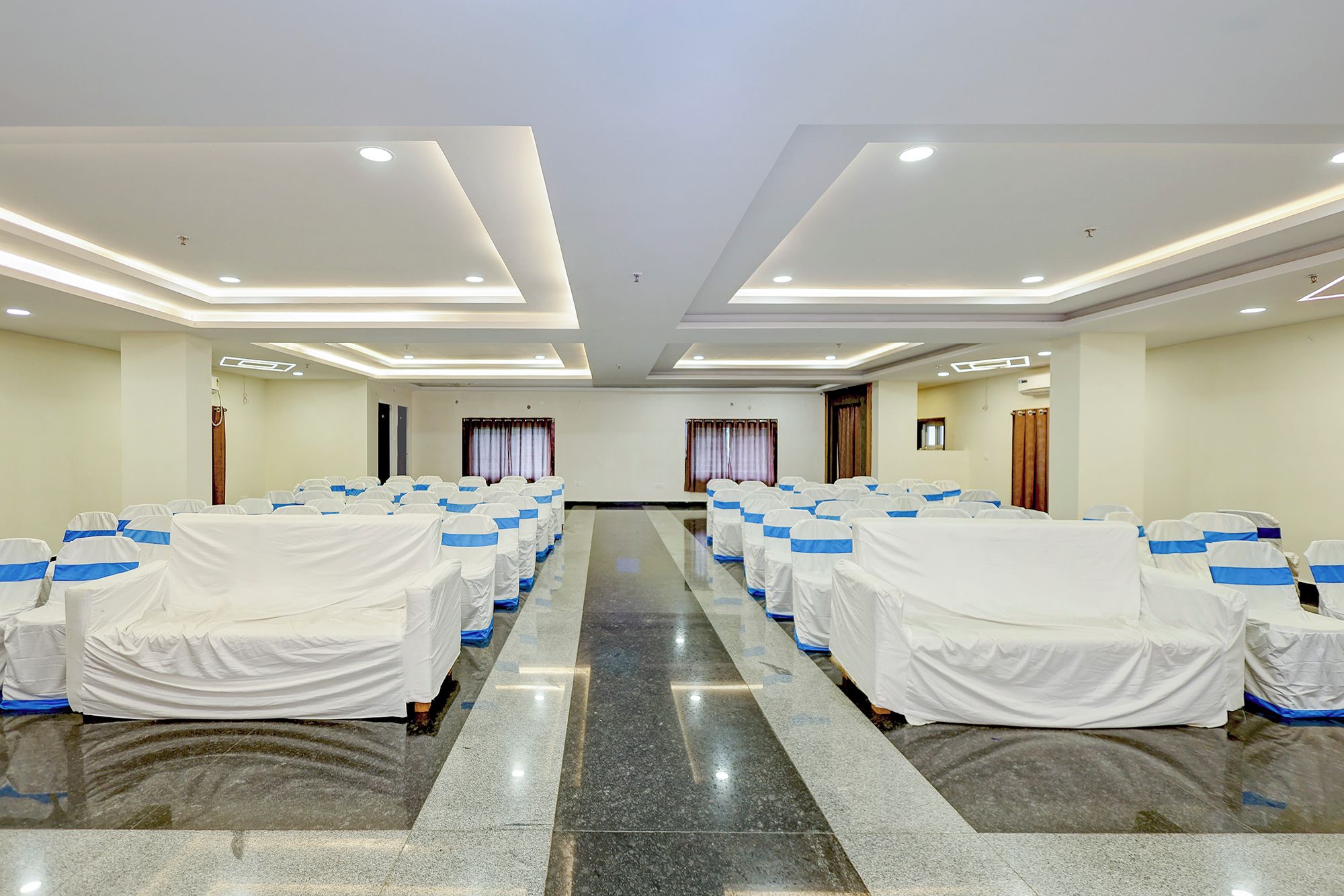 Un salón de conferencias con filas de sillas cubiertas en blanco y azul, un suelo pulido e iluminación empotrada en el techo.