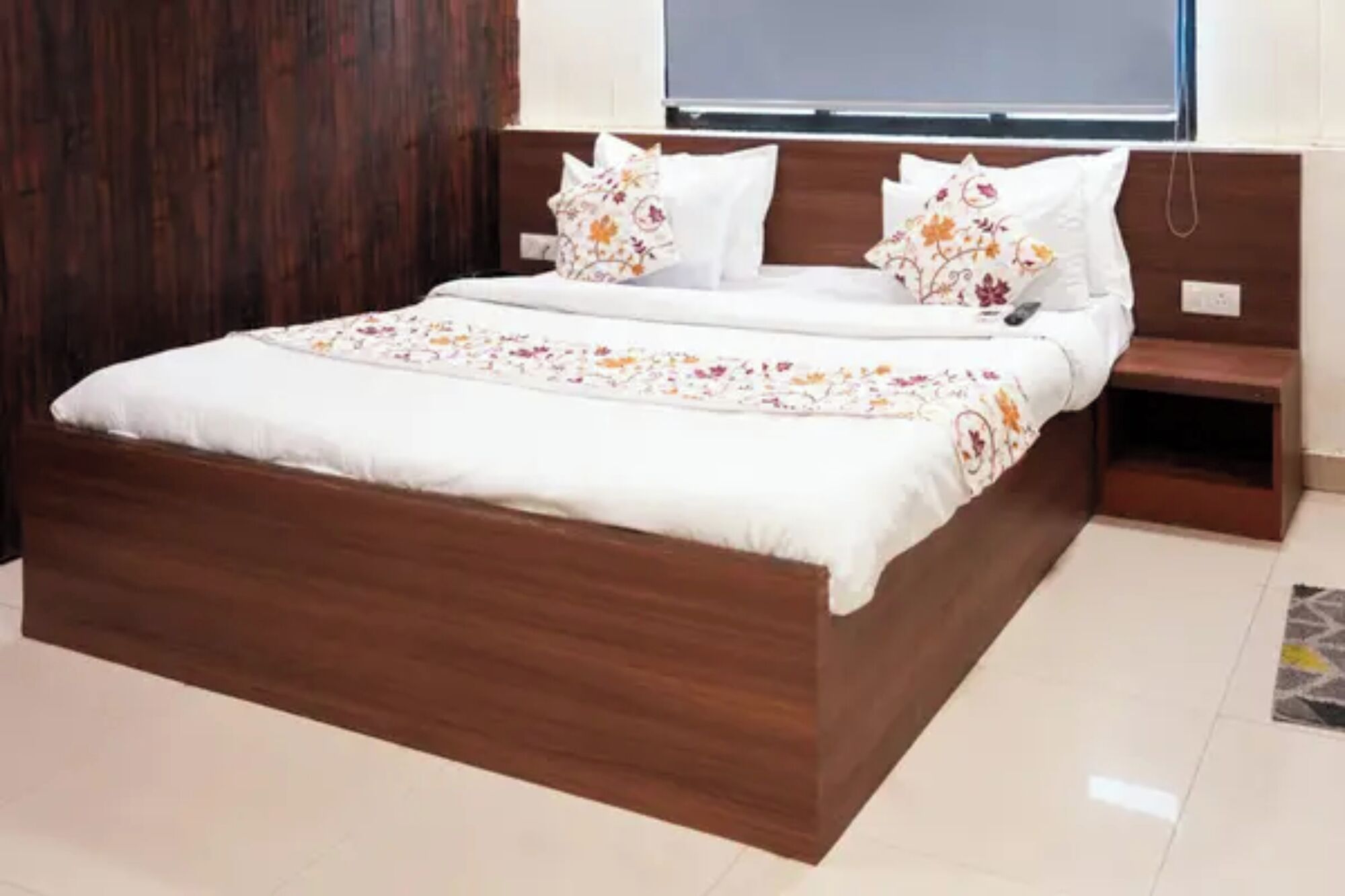 Ein Doppelbett mit hölzernem Gestell, weißer Bettwäsche und Kissen mit Blumenmuster.