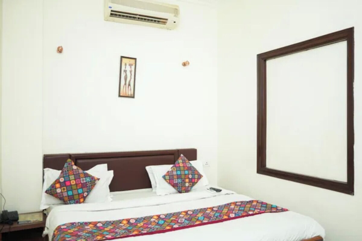 Una habitación de hotel con una cama, una mesita de noche, aire acondicionado instalado en la pared y un cuadro enmarcado.