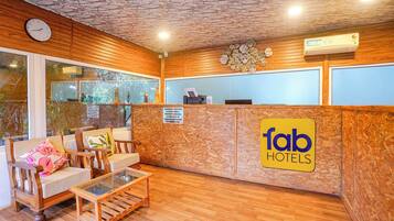 Zona de recepción con un mostrador de madera, un reloj y un área de descanso con una mesa de vidrio y sillas.