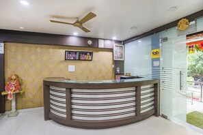 A reception area with a curved counter, ceiling fan, and framed photos on the wall. - FabHotel Ashoka Palace (Bhopal)