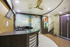 A reception area with a curved desk, a ceiling fan, and a staircase leading to an upper level. - FabHotel Ashoka Palace (Bhopal)