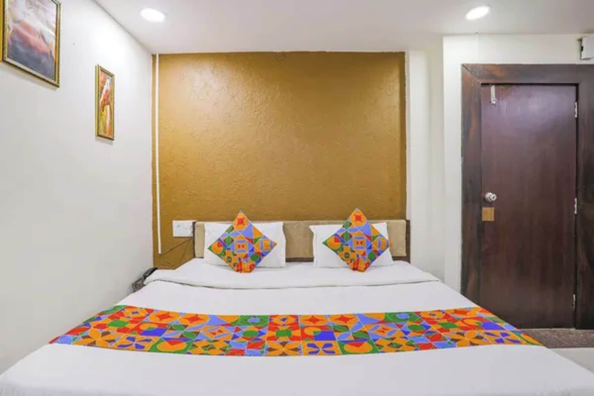 Ein Hotelzimmer mit Bett, Kopfteil, Tür und einer Wand mit zwei gerahmten Bildern.