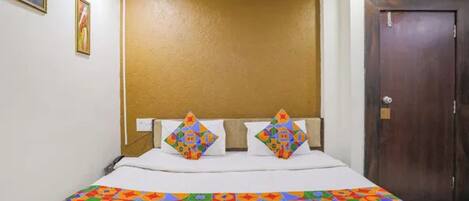 Quarto de hotel com cama, cabeceira, porta e parede com duas imagens emolduradas.