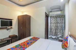 A hotel room with a bed, a TV mounted on the wall, a wardrobe, and a curtain with a circular pattern. - FabHotel Ashoka Palace (Bhopal)