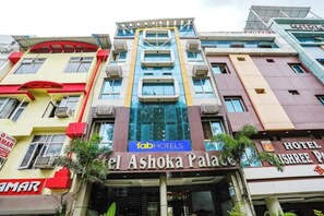 Un edificio de hotel de varios pisos con un letrero destacado de 'FabHotels' y 'Hotel Ashoka Palace'.