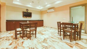 A dining area with a marble floor, wooden chairs, a table, a ceiling fan, and a mounted television. - Fabhotel Prime Asl (Kolkata)