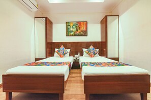 A hotel room with two beds, a wooden headboard, a painting above the beds, and a small table between the beds.