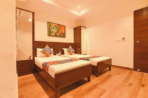 A hotel room with two beds, a wooden floor, a painting on the wall, and a door.