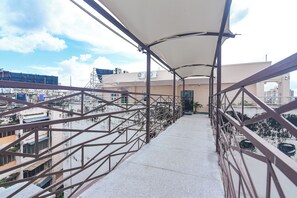 A covered balcony with metal railings, a concrete floor, and a view of buildings in the background.