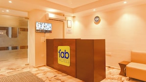 A reception area with a marble floor, a reception desk, a television mounted on the wall, and a clock. - Fabhotel Prime Asl (Kolkata)