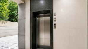 An elevator with a metallic finish, set within a wall with patterned tiles and a contrasting dark base. - Fabhotel Prime Asl (Kolkata)
