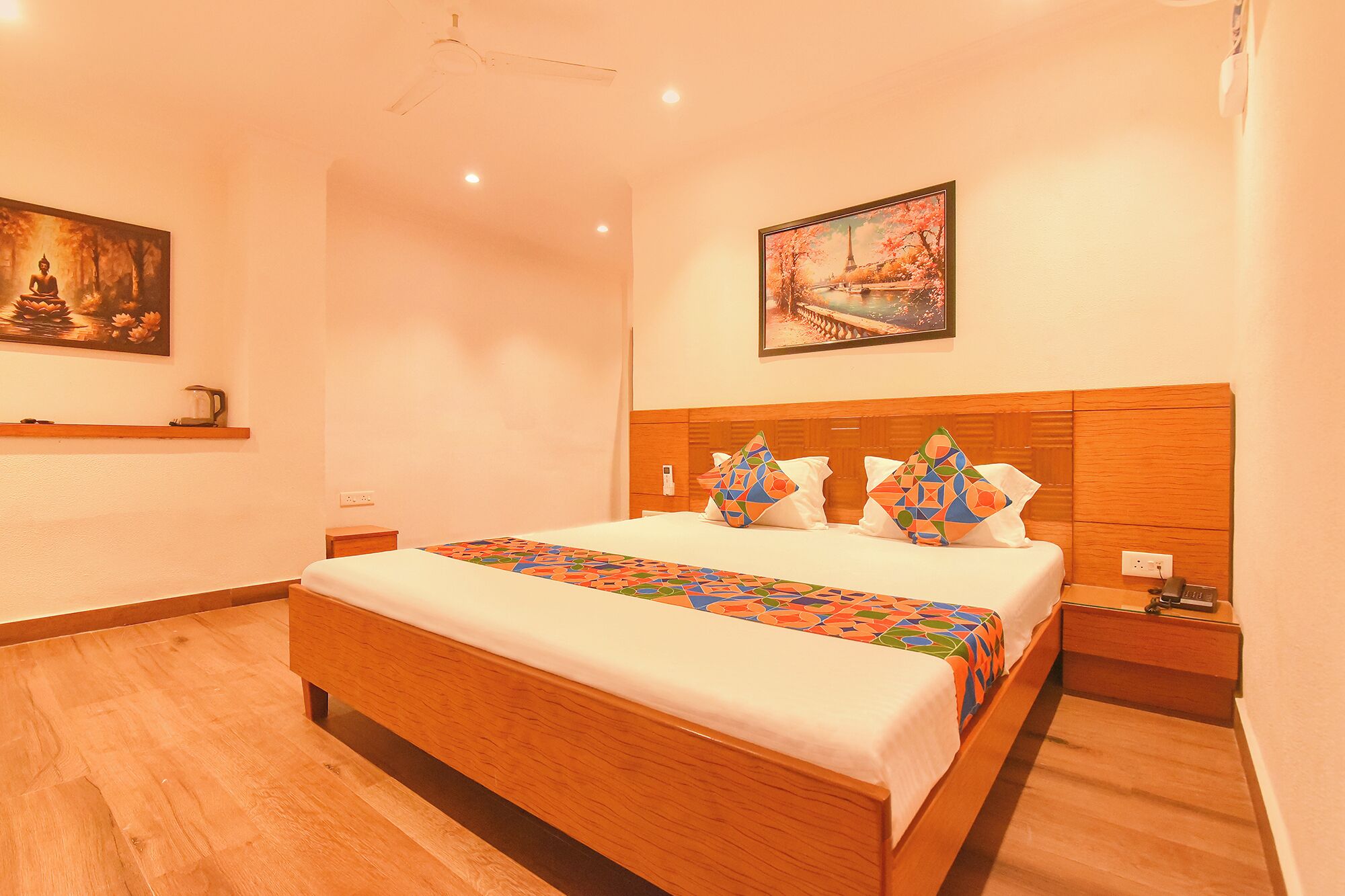 A hotel room with a wooden bed, a nightstand, a painting of a Buddha, and a painting of a bridge.