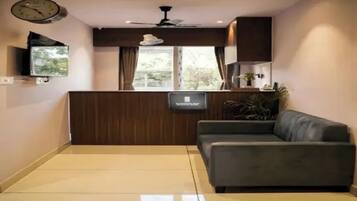 Un salon avec un canapé, un téléviseur fixé au mur, un ventilateur de plafond et une fenêtre avec des rideaux.