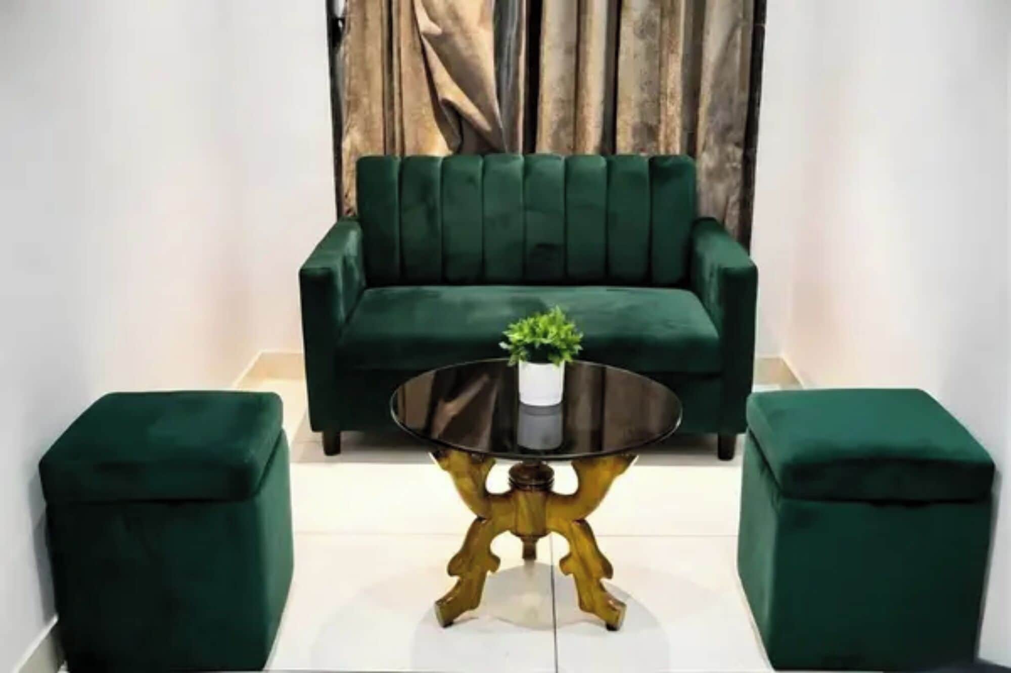Ein grünes Sofa, ein runder Tisch mit einer Pflanze und passende Hocker in einem Raum mit Holzwand.