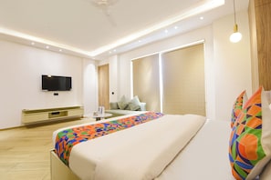 Una habitación de hotel moderna con una cama, televisor, sofá y un ventanal grande.