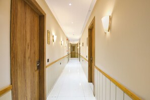 Un pasillo de hotel con puertas de madera, paredes blancas e iluminación.