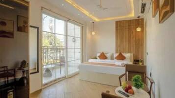 Quarto de hotel com cama, uma mesinha com frutas, uma cadeira e varanda com guarda-corpo.