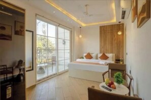Una habitación de hotel con cama, una mesita con frutas, una silla y un balcón con barandilla.