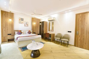 A hotel room with a bed, a desk, two chairs, a round table, a ceiling fan, and an air conditioning unit. - FabHotel Prime Da Marion (New Delhi)