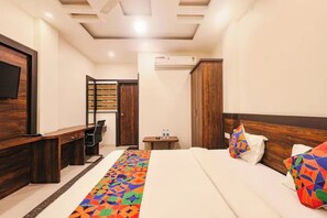 Habitación de hotel con cama, escritorio, silla, televisor y aire acondicionado.