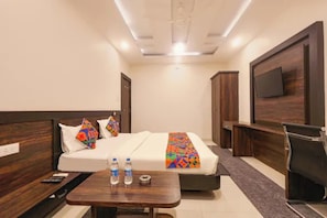 Quarto de hotel com cama, mesas de cabeceira, televisão e escrivaninha.