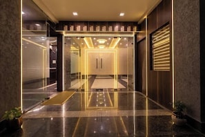 Un vestíbulo moderno con entrada de vidrio, piso de mármol pulido y una lámpara central.