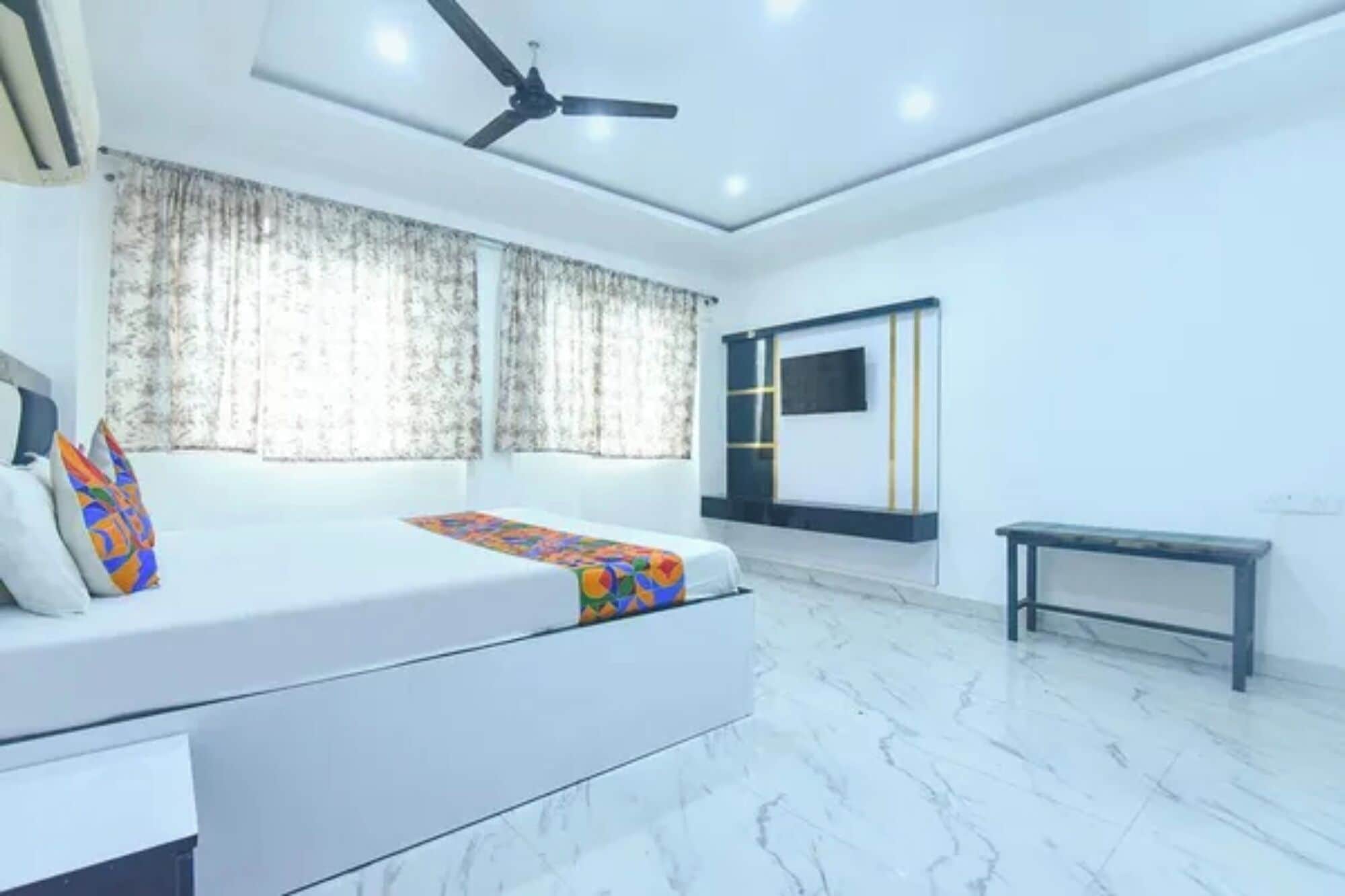 Un dormitorio moderno con cama, ventilador de techo, televisión y un banco.
