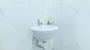 Un baño con lavamanos blanco, espejo y dispensador de jabón sobre una pequeña estantería.