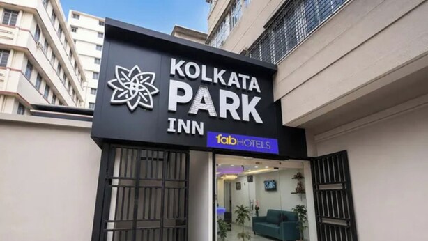 Exterior del Kolkata Park Inn, con fachada moderna, logotipo destacado, entrada protegida por un portón y un interior visible con sofás y plantas en macetas.