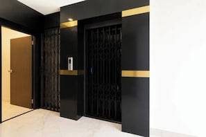 A hallway with a black door, a black gate, and a small electronic device on the wall. - FabHotel Kolkata Park Inn (Kolkata)
