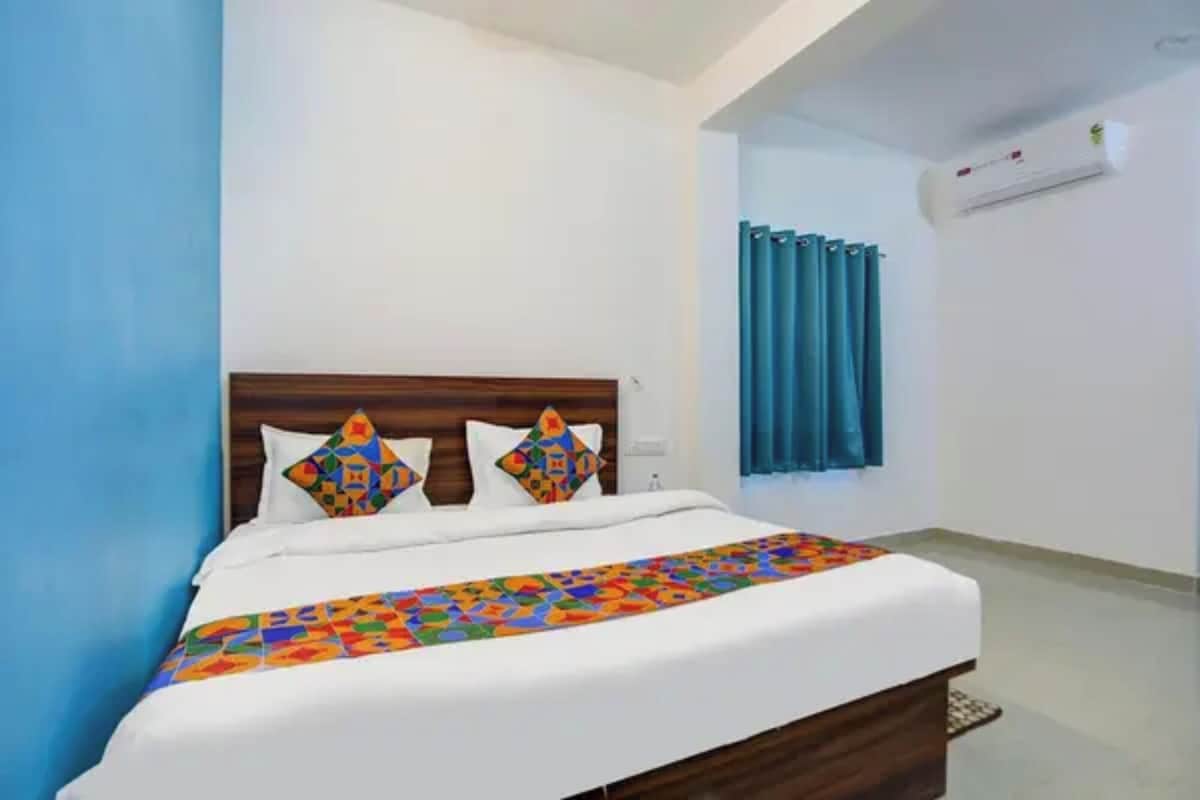 Quarto de hotel com cama, cabeceira, janela com cortinas e aparelho de ar condicionado.