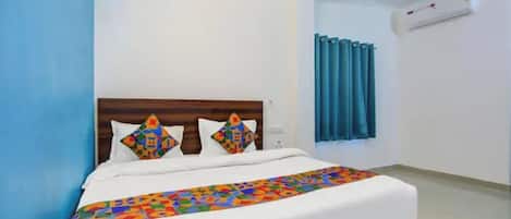 Habitación de hotel con una cama, cabecera, ventana con cortinas y equipo de aire acondicionado.