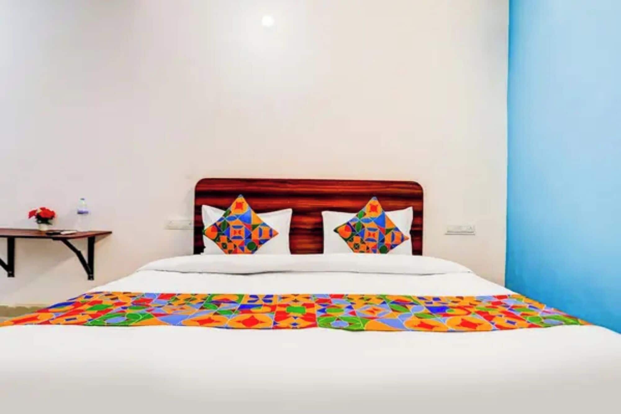 A hotel room with a bed, two pillows with geometric patterns, a bedside table with a vase of flowers, and a water bottle.