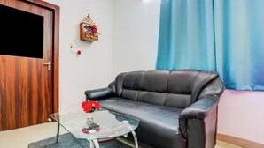 Una sala de estar con un sofá de cuero, una mesa de centro de vidrio, una puerta de madera y un adorno fijado a la pared.