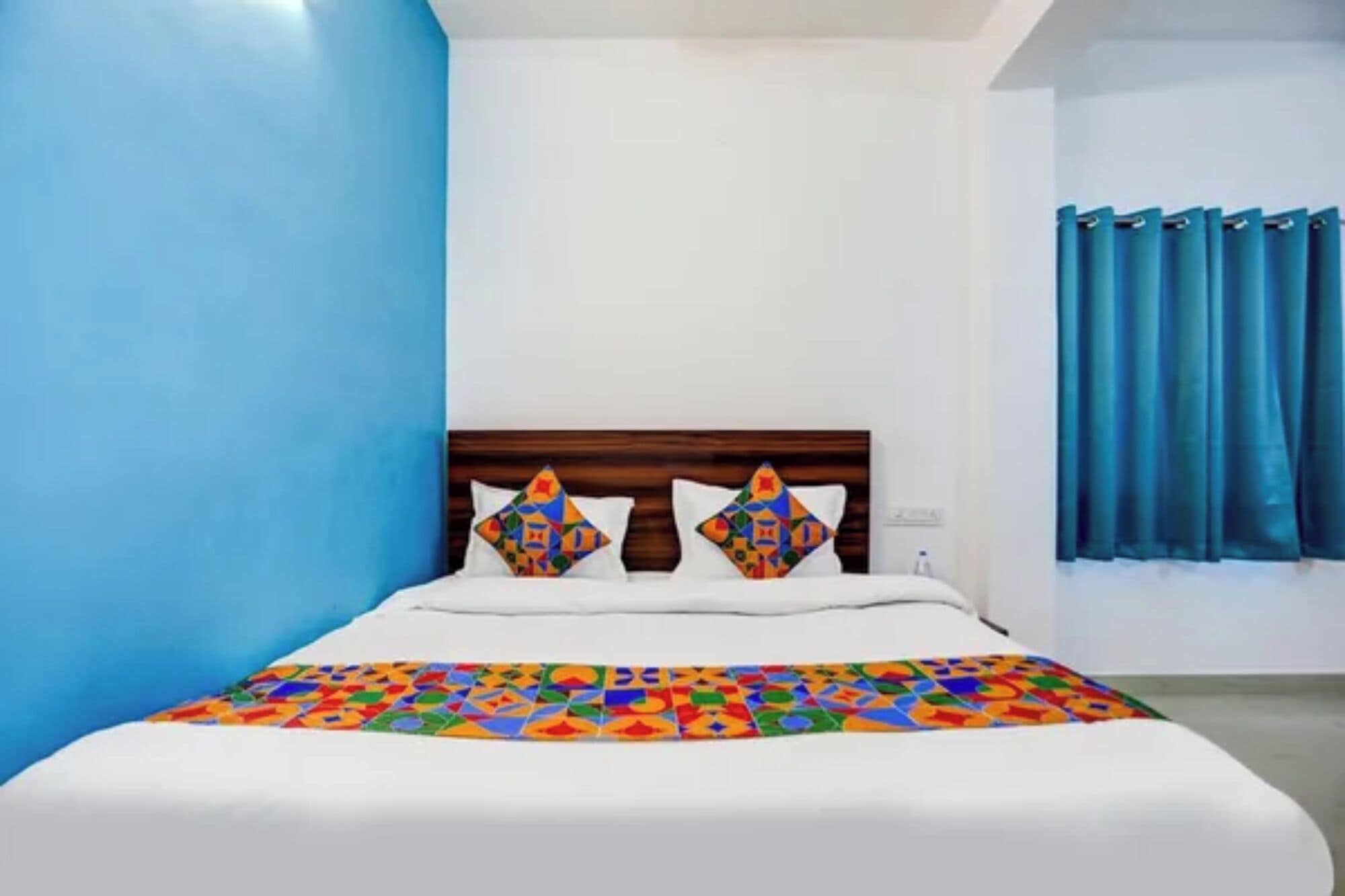 A hotel room with a bed, a headboard, a blue wall, and a window with curtains.