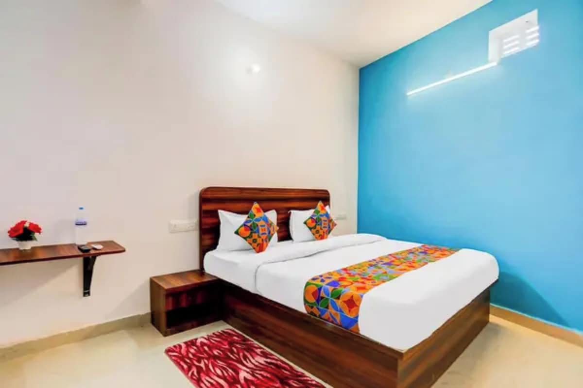 Quarto de hotel com cama de madeira, mesa de cabeceira e uma garrafa de água, além de um tapete vermelho.