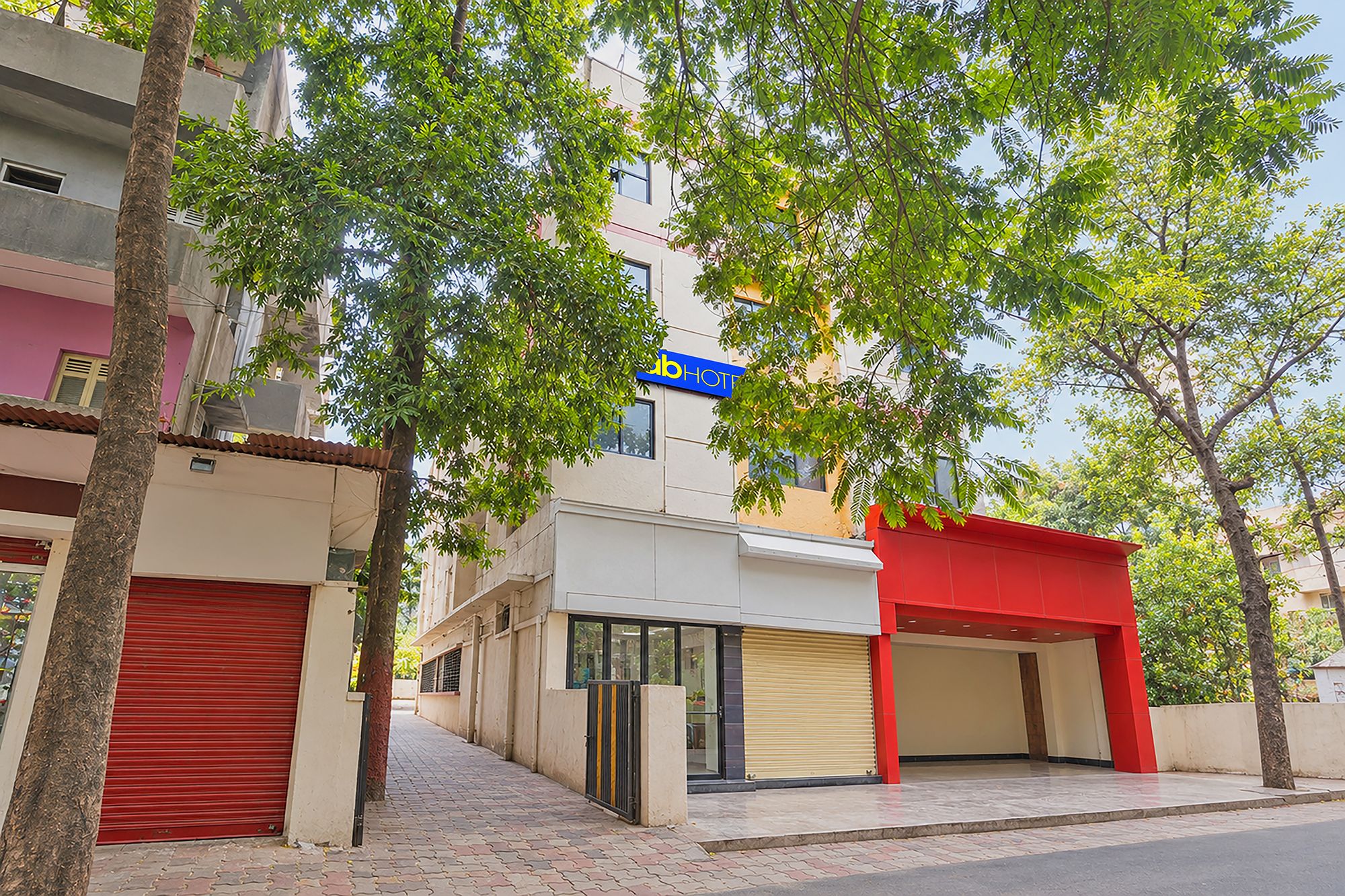 Un hotel con entrada roja, un letrero azul y una calle bordeada de árboles.