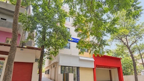 Un hotel con entrada roja, un letrero azul y una calle bordeada de árboles.
