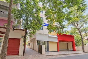 A hotel with a red entrance, a blue sign, and a tree-lined street. - Fabhotel Sai Seva (Nashik)