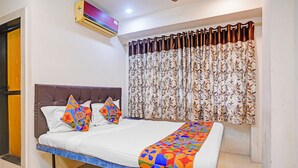 Una habitación con una cama, ventana con cortinas, equipo de aire acondicionado y una puerta.