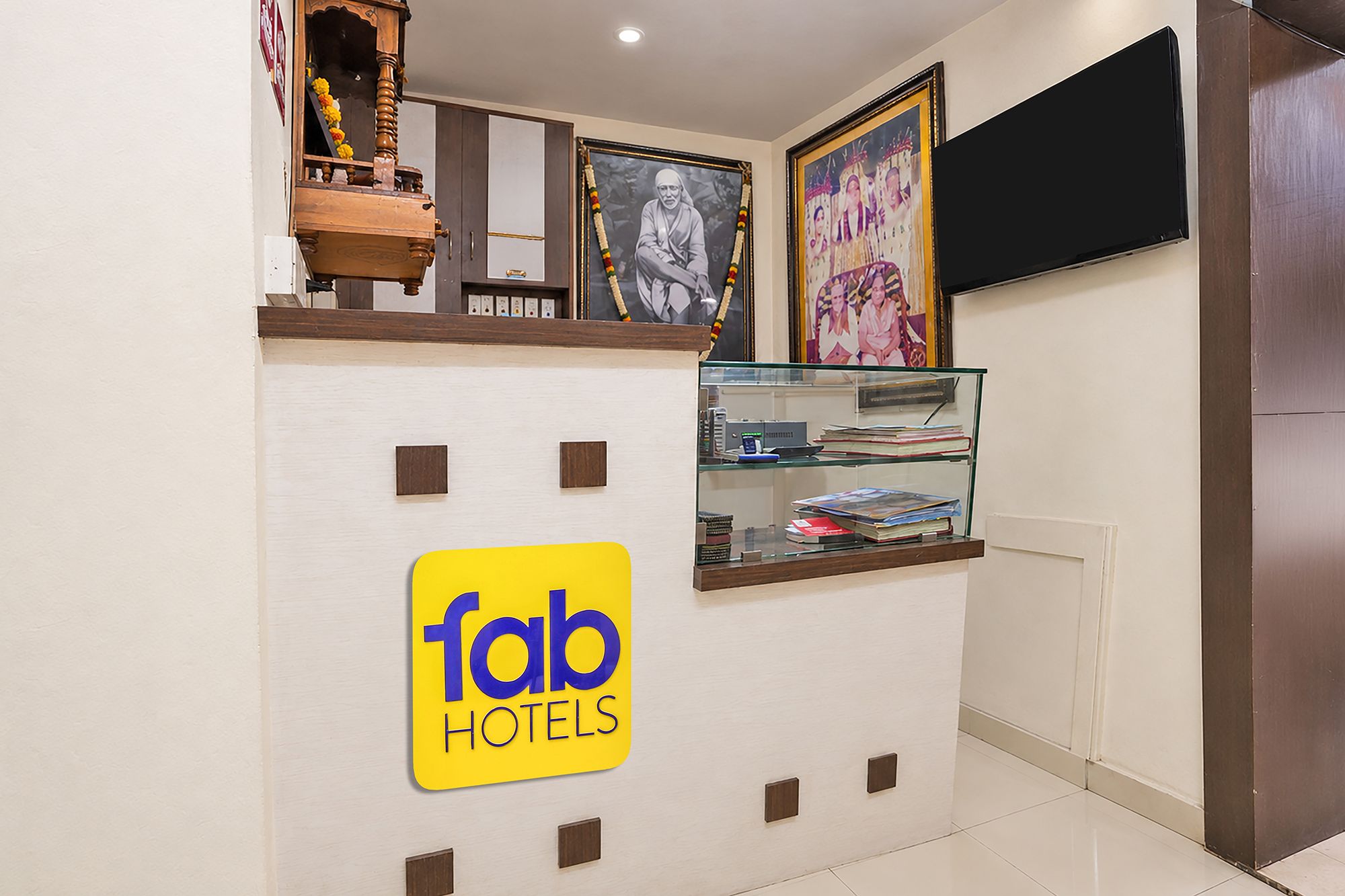 Et receptionsområde med et 'fab hotels' skilt, et fjernsyn ophængt på væggen og en glasmontre med bøger.