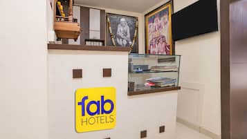 Et receptionsområde med et 'fab hotels' skilt, et fjernsyn ophængt på væggen og en glasmontre med bøger.