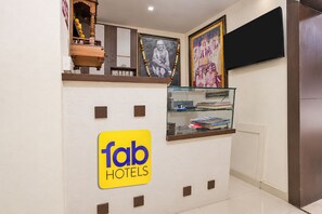 A reception area with a 'fab hotels' sign, a television mounted on the wall, and a glass display case with books. - FabHotel Sai Seva (Nashik)