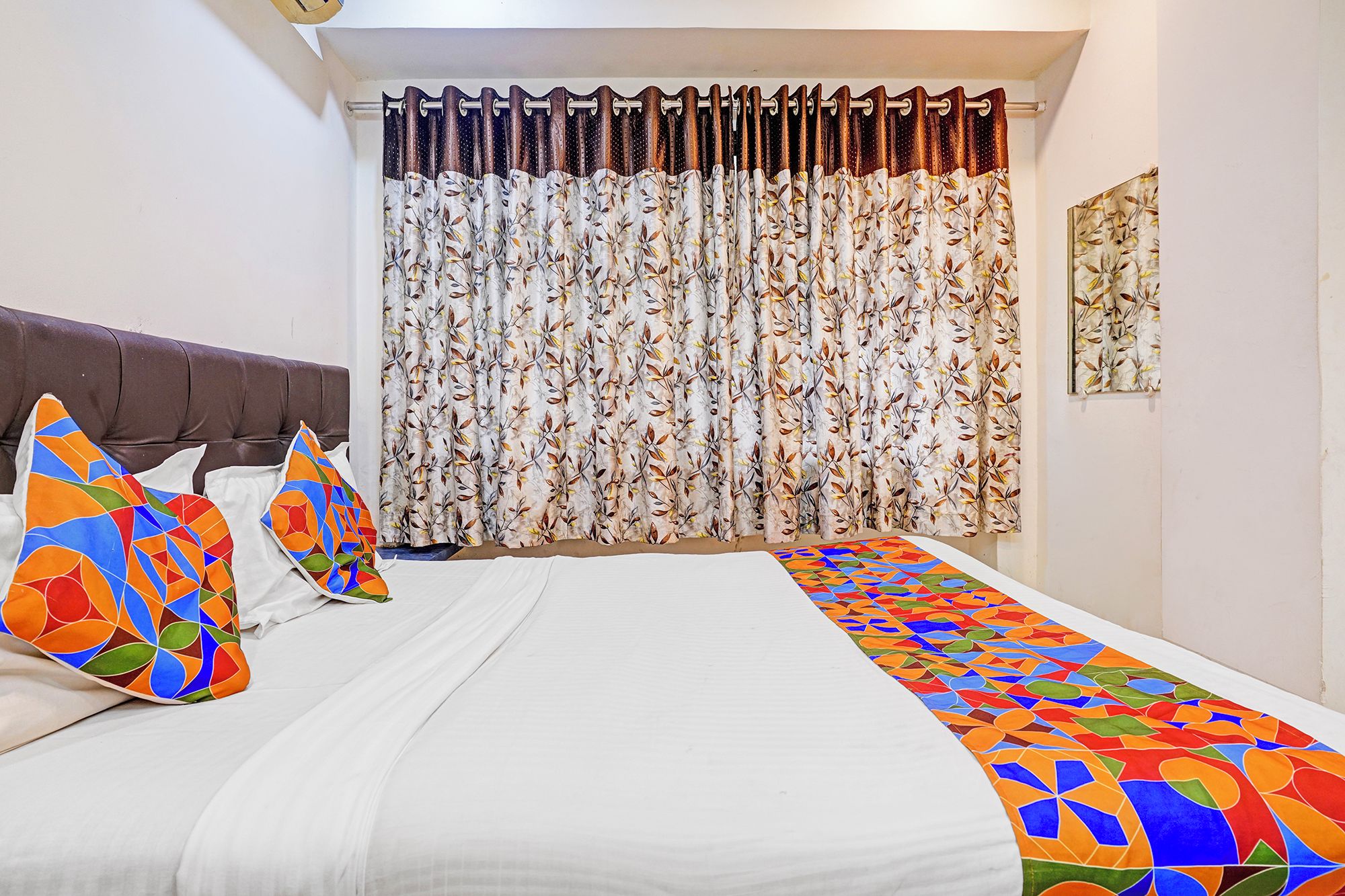 A hotel room with a bed, pillows, a curtain, and a wall-mounted artwork.