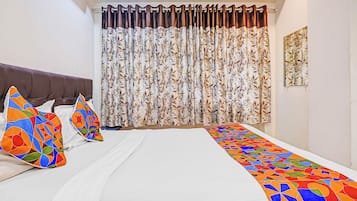 A hotel room with a bed, pillows, a curtain, and a wall-mounted artwork.