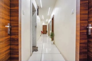 Un pasillo con una puerta de madera a la izquierda, una pared blanca y una planta en maceta a la derecha.